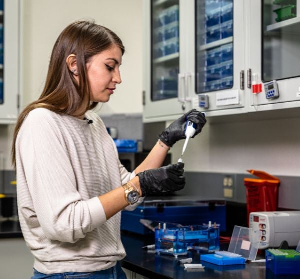 Woman holding a syringe over a petri dish in a lab environment